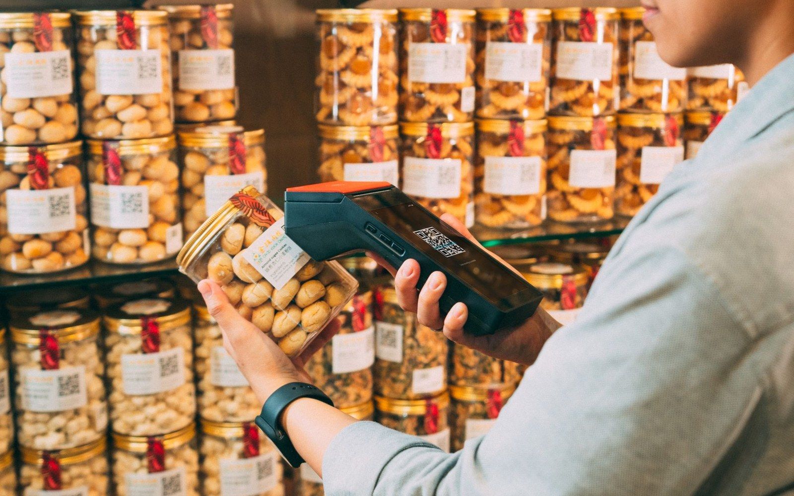 Someone scans a jarred snack's QR code label with a handheld barcode reader in a shop