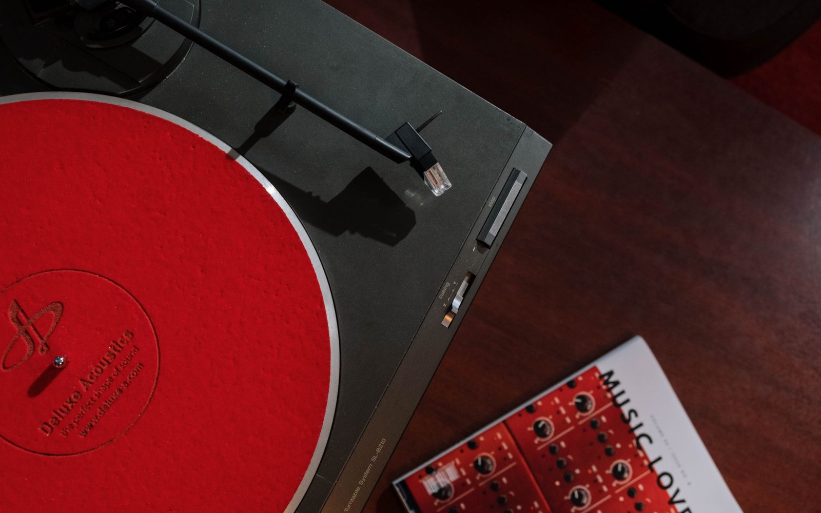 Turntable with red felt mat sits beside a record sleeve on a wooden table