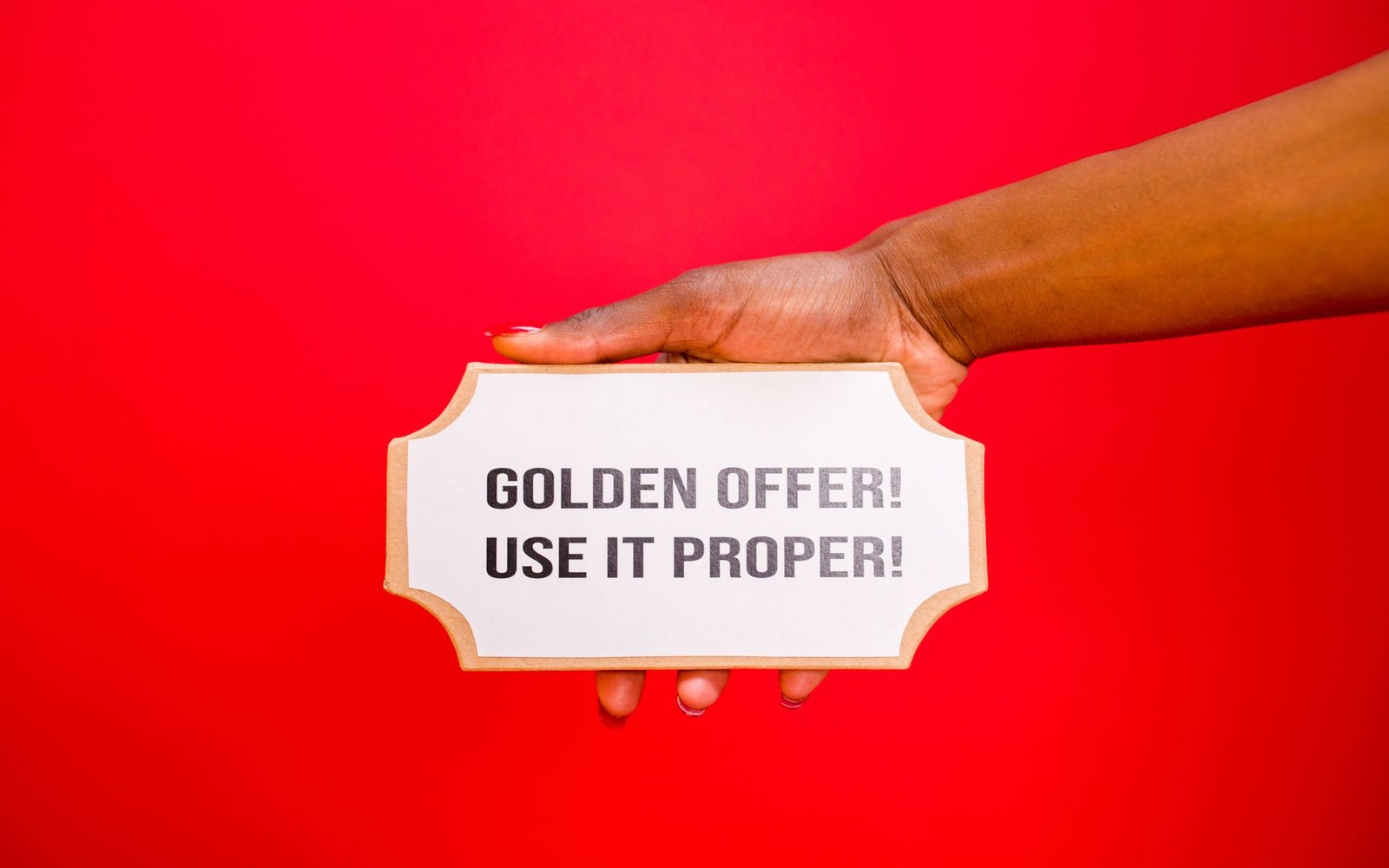 A hand holds a ticket-shaped card reading "golden offer! use it proper!" against a red background